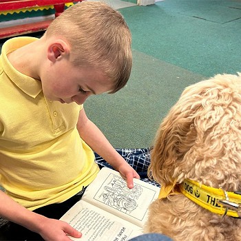 A boy reading a book to Ned in the classroom