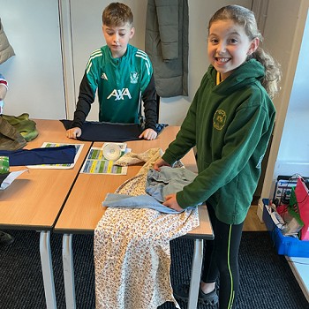 2 fyfyriwr yn mesur eu ffabrigau ar fwrdd