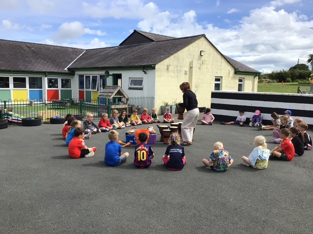 Plant blwyddyn 1 yn eistedd ar y llawer ac yn gwrando ar athrawes