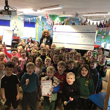 Year 1 and 2 children standing infront of the person holding a big cheque