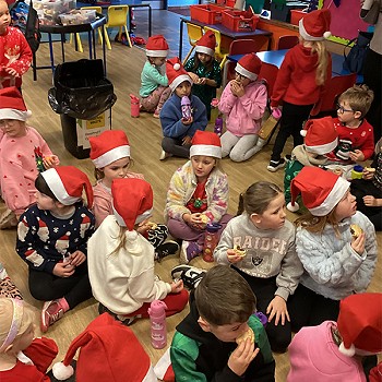 Golwg agos ar y plant yn gwisgo hetiau coch Siôn Corn ac yn bwyta mins peis yn y dosbarth