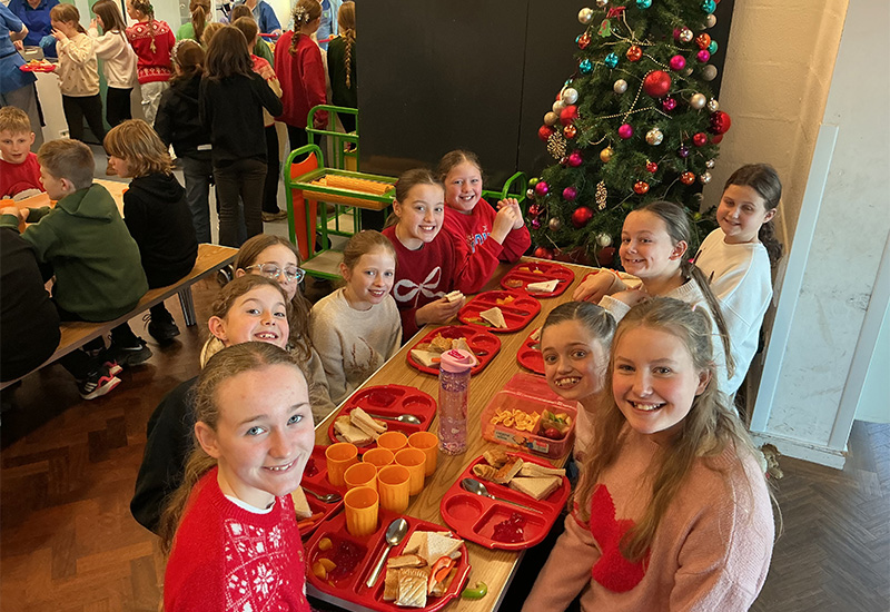 Grwp o ferched o gwmpas bwrdd yn mwynhau te nadolig