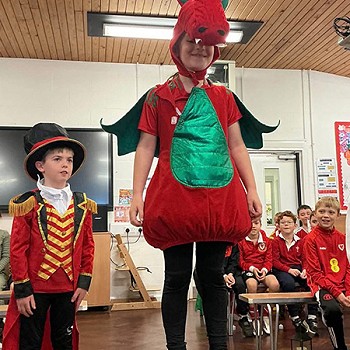 Plentyn yn sefyll ar gadair wedi gwisgo fynu fel y draig goch