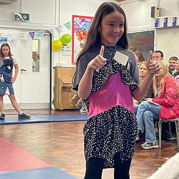 A child posing to show the clothes she is wearing while putting thumbs up
